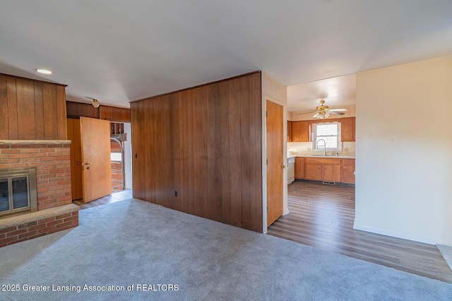 unfurnished living room with carpet floors, a fireplace, a ceiling fan, and a sink