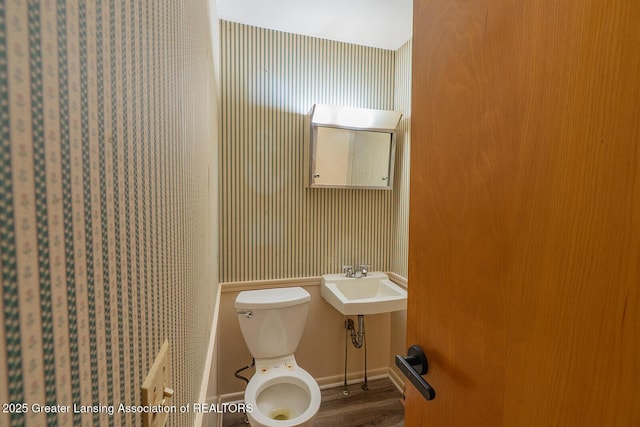 half bath featuring toilet, wallpapered walls, and a sink