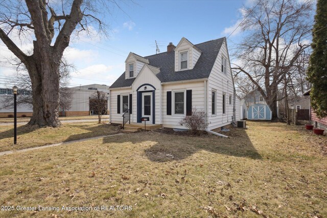 cape cod home with an outbuilding, a front yard, roof with shingles, a chimney, and a storage shed