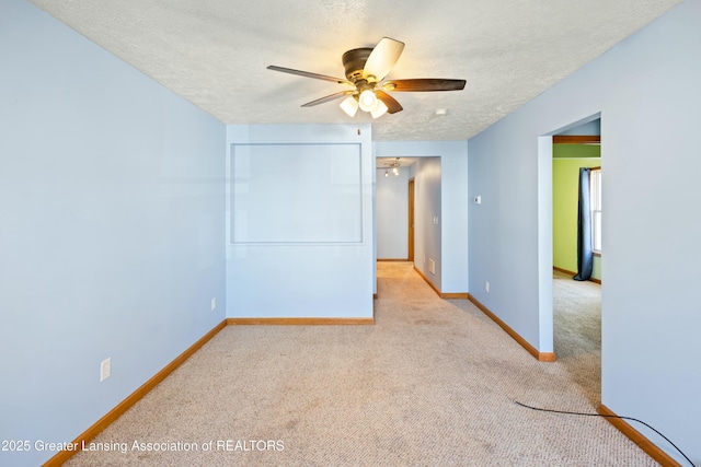 empty room featuring a textured ceiling, carpet, baseboards, and a ceiling fan
