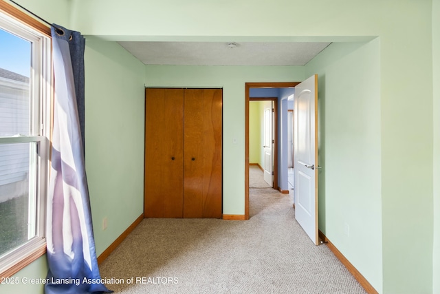 unfurnished bedroom with a closet, baseboards, and light colored carpet