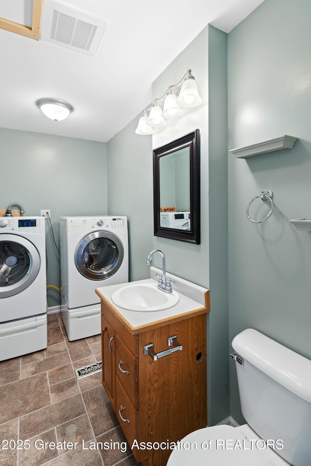 half bath featuring vanity, toilet, stone finish floor, washing machine and clothes dryer, and visible vents
