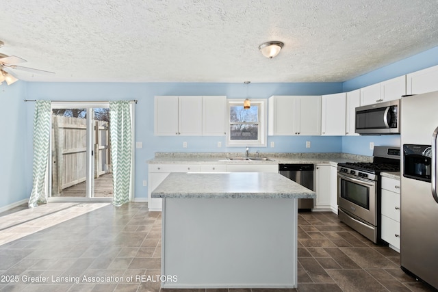 kitchen featuring a kitchen island, a sink, white cabinets, a ceiling fan, and appliances with stainless steel finishes