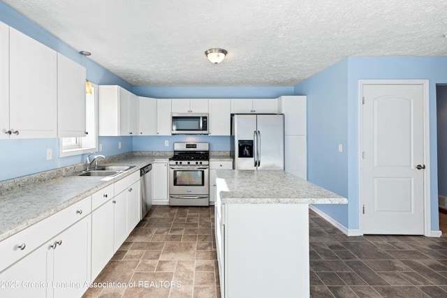 kitchen with light countertops, white cabinets, stainless steel appliances, a sink, and a center island