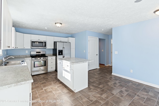 kitchen featuring light countertops, white cabinets, a kitchen island, appliances with stainless steel finishes, and a sink
