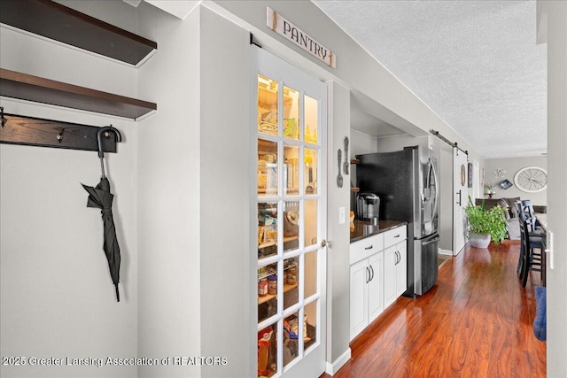13305 Nelson, Bath, MI 48808 - kitchen featuring dark wood-style flooring, a textured ceiling, freestanding refrigerator, dark countertops, and a barn door