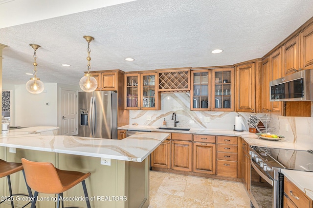 13600 Forest Hill Rd, Grand Ledge, MI 48837 - kitchen featuring stainless steel appliances, a sink, brown cabinetry, light stone countertops, and decorative backsplash