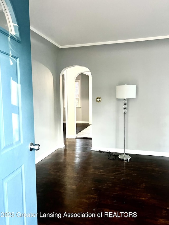 909 Britten Ave, Lansing, MI 48910 - empty room featuring dark wood finished floors, arched walkways, baseboards, and ornamental molding