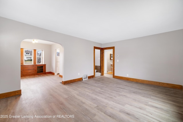 spare room featuring baseboards, wood finished floors, and arched walkways