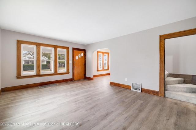 unfurnished living room with stairs, wood finished floors, baseboards, visible vents, and arched walkways