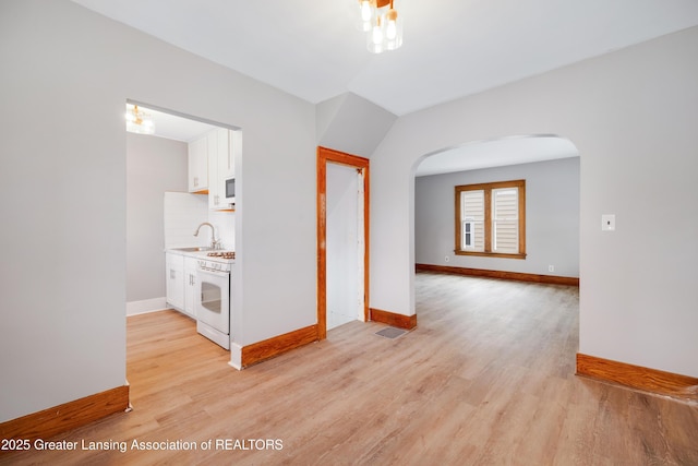 empty room featuring arched walkways, visible vents, baseboards, and light wood finished floors
