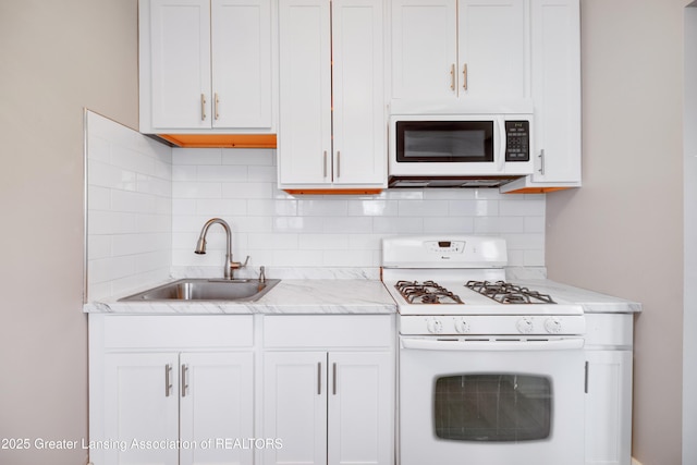 kitchen with white appliances, backsplash, a sink, white cabinets, and light stone countertops