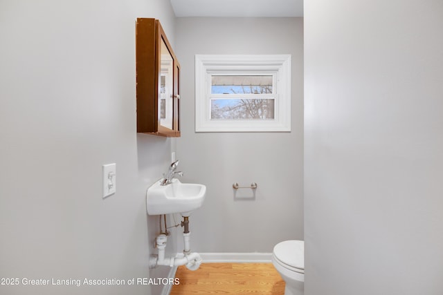 bathroom with baseboards, wood finished floors, toilet, and a sink