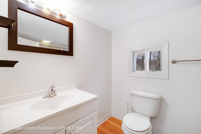 bathroom with baseboards, wood finished floors, toilet, and vanity