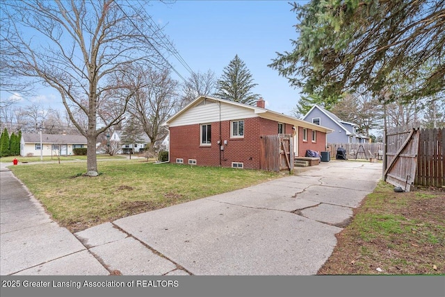 view of side of home with driveway, fence, a chimney, brick siding, and a lawn
