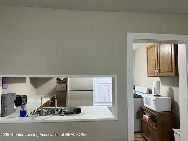 kitchen with light countertops, a sink, white microwave, washer / dryer, and freestanding refrigerator