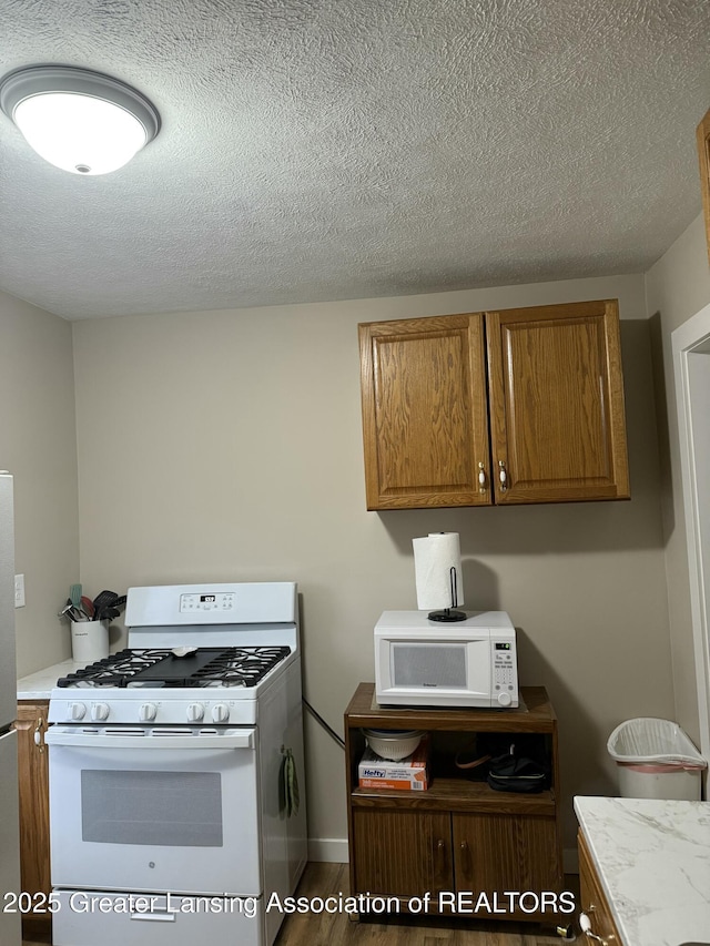kitchen with light countertops, wood finished floors, a textured ceiling, brown cabinets, and white appliances