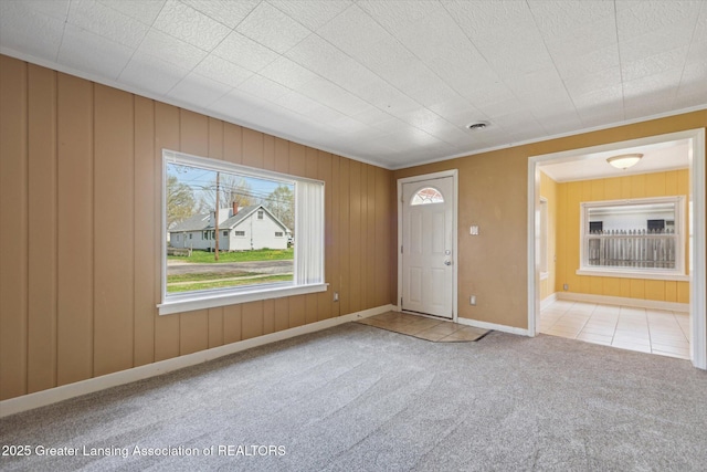 foyer entrance with baseboards, crown molding, tile patterned flooring, and carpet