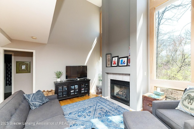 living area with a tiled fireplace, wood finished floors, and a high ceiling