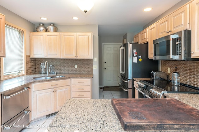 kitchen featuring light stone counters, a sink, appliances with stainless steel finishes, light brown cabinets, and light tile patterned flooring
