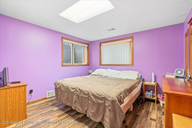 bedroom featuring baseboards, visible vents, wood finished floors, and a drop ceiling