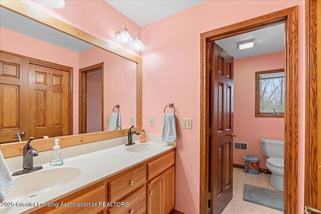 full bath featuring toilet, a sink, double vanity, and baseboards