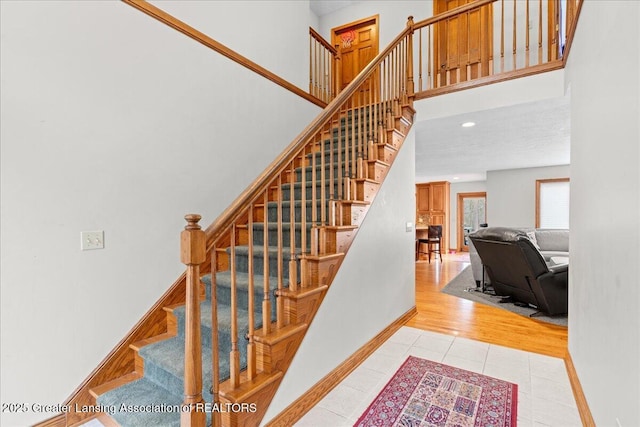 stairs with baseboards, a towering ceiling, recessed lighting, and tile patterned flooring