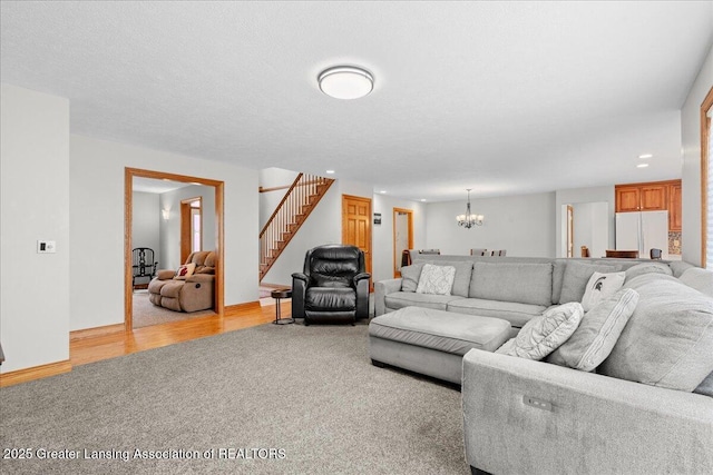 living area featuring a textured ceiling, baseboards, stairs, a notable chandelier, and light colored carpet