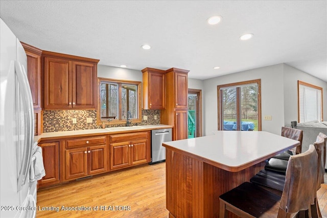 kitchen featuring light countertops, a breakfast bar, a sink, stainless steel dishwasher, and freestanding refrigerator