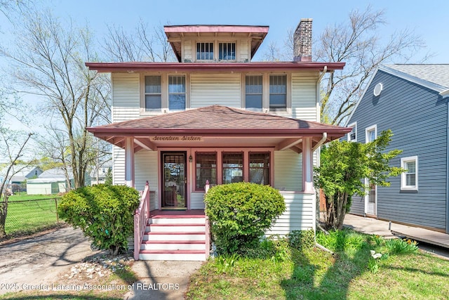 american foursquare style home with a shingled roof, a chimney, covered porch, and fence