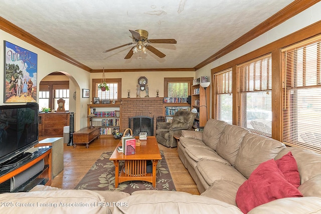 living room with a brick fireplace, wood finished floors, arched walkways, a textured ceiling, and ceiling fan