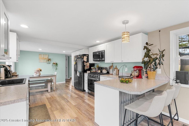 kitchen with light countertops, a peninsula, appliances with stainless steel finishes, white cabinetry, and a sink