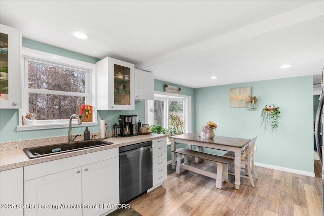 kitchen featuring light countertops, a sink, dishwasher, light wood-style flooring, and white cabinets