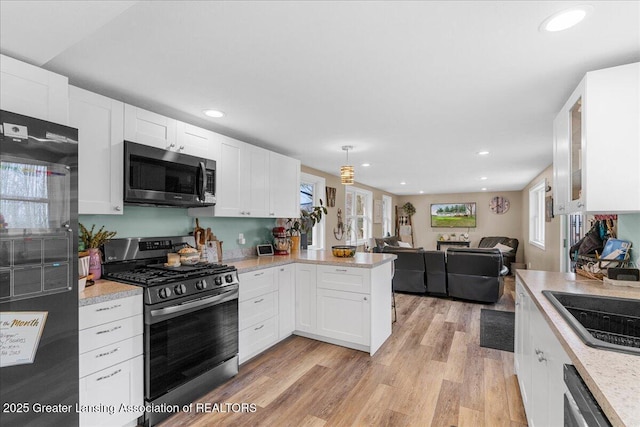 kitchen with white cabinetry, light countertops, light wood-type flooring, stainless steel appliances, and a peninsula