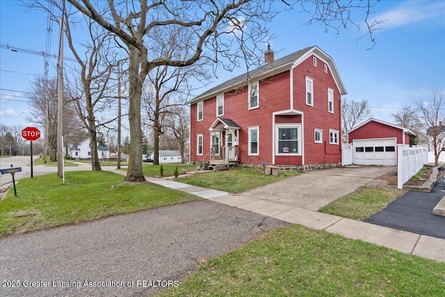 view of front facade with a chimney, an outbuilding, aphalt driveway, a front lawn, and a detached garage