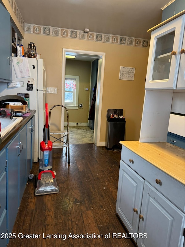kitchen with a sink, freestanding refrigerator, baseboards, wood counters, and dark wood-style flooring