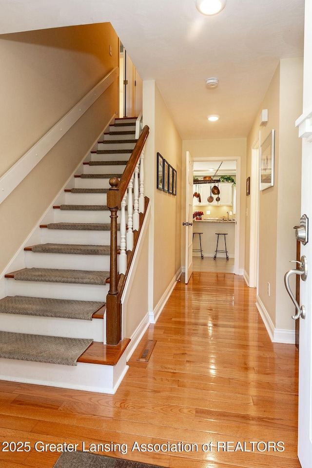 hall with baseboards, stairs, light wood finished floors, and visible vents