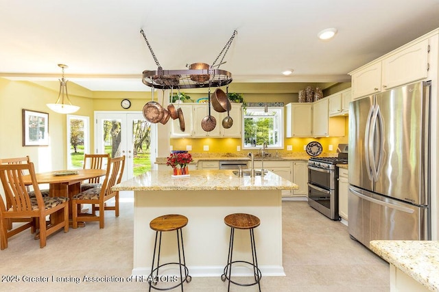 kitchen featuring french doors, a kitchen bar, an island with sink, a sink, and appliances with stainless steel finishes
