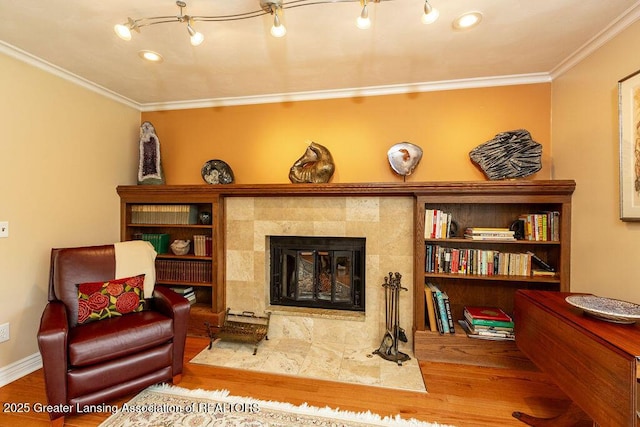 living area featuring a tiled fireplace, crown molding, and wood finished floors