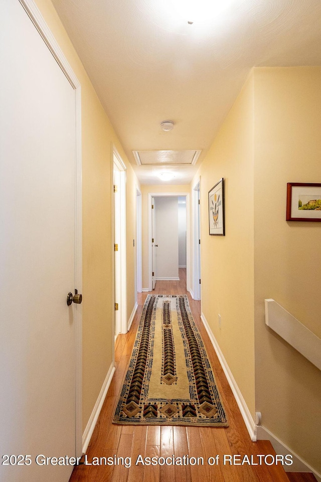 hall with attic access, wood finished floors, and baseboards
