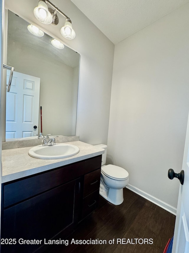2632 Carnoustie Dr, Okemos, MI 48864 - half bath featuring vanity, baseboards, a textured ceiling, toilet, and wood finished floors