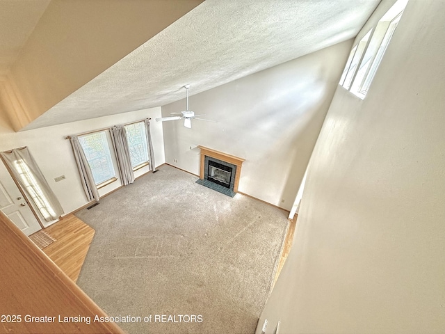 1970 Hollowbrook Dr, Holt, MI 48842 - unfurnished living room featuring a fireplace with raised hearth, a textured ceiling, a ceiling fan, a healthy amount of sunlight, and vaulted ceiling