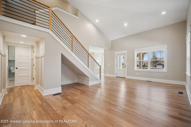 foyer entrance featuring light wood-type flooring, a towering ceiling, baseboards, and stairs