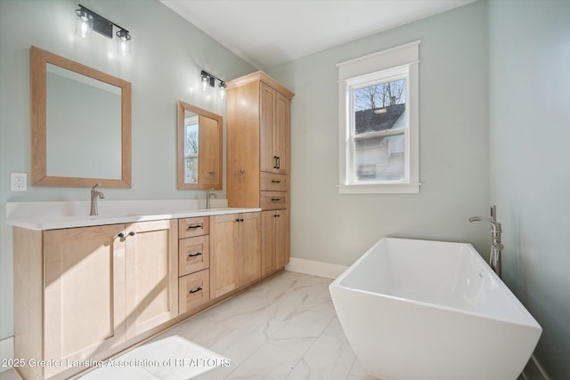 full bath featuring a freestanding tub, baseboards, double vanity, marble finish floor, and a sink