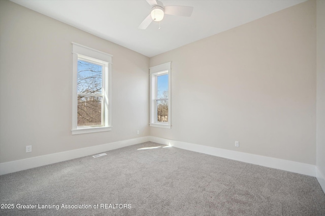 carpeted spare room with visible vents, baseboards, and ceiling fan