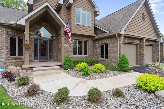 5810 Caleta Dr, Lansing, MI 48911 - view of exterior entry with brick siding, a garage, a shingled roof, and driveway