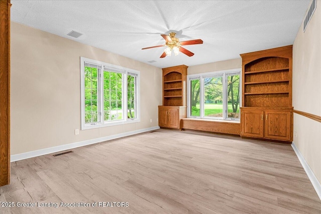 4345 Courtside Dr, Williamston, MI 48895 - unfurnished living room featuring baseboards, light wood-type flooring, a ceiling fan, built in shelves, and a textured ceiling