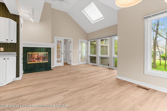 4345 Courtside Dr, Williamston, MI 48895 - unfurnished living room featuring a skylight, light wood-type flooring, high vaulted ceiling, a tile fireplace, and baseboards