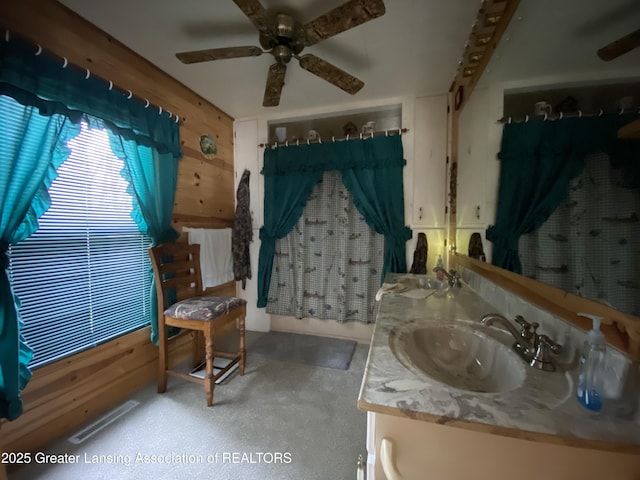 sitting room featuring wooden walls, visible vents, ceiling fan, and light carpet