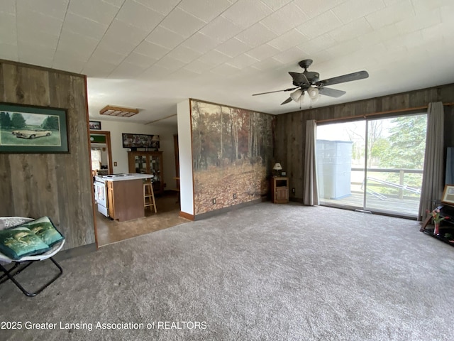 unfurnished living room with wood walls, a ceiling fan, and carpet floors